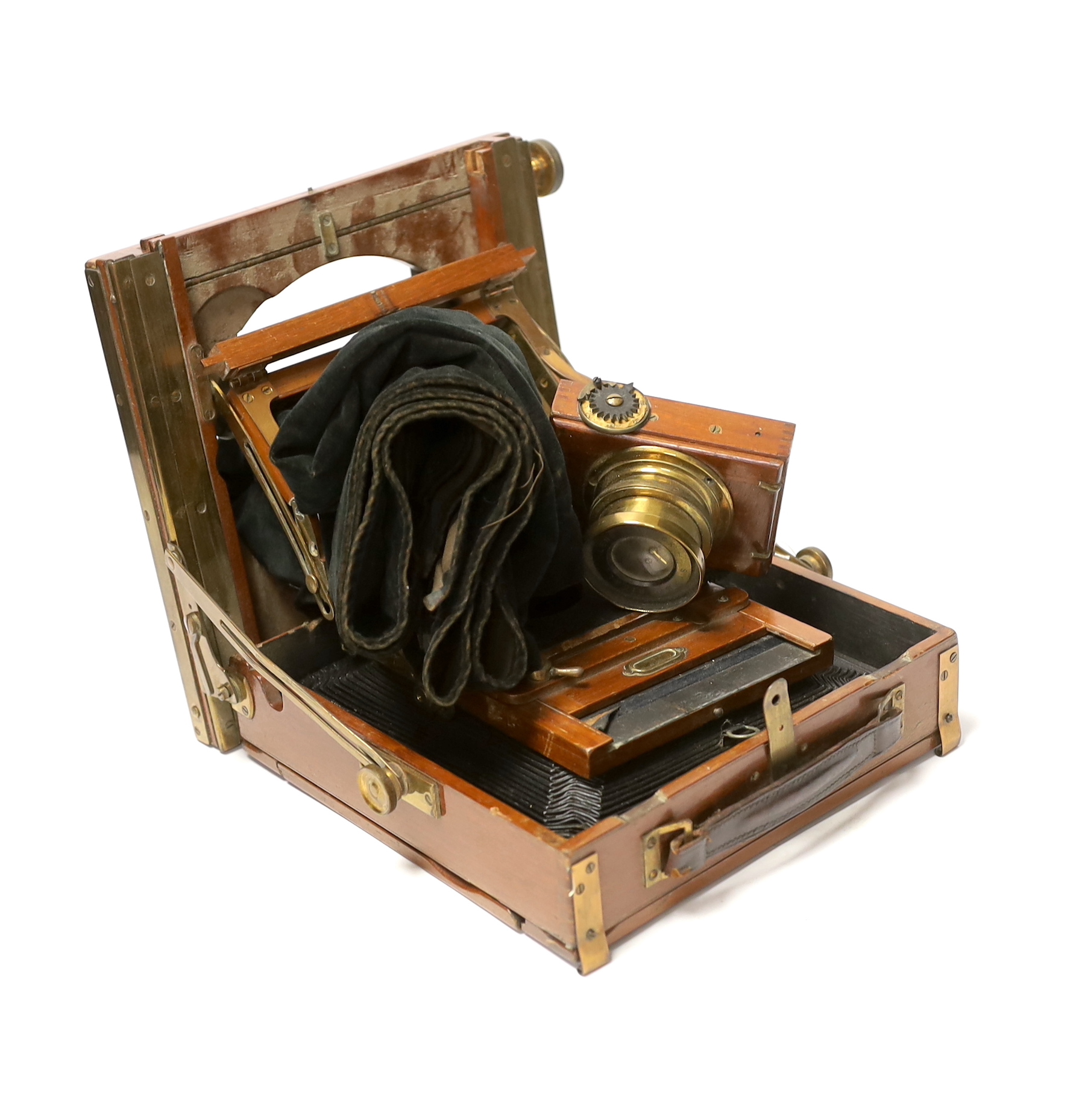 An early 20th century brass and mahogany half plate bellows camera with a lens and a shutter action by Thornton Pickard, on an oak tripod